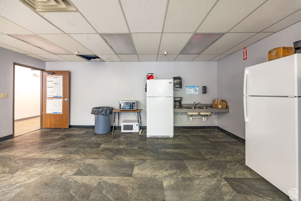 Kitchen featuring freestanding refrigerator, a drop ceiling, and stone finish floors