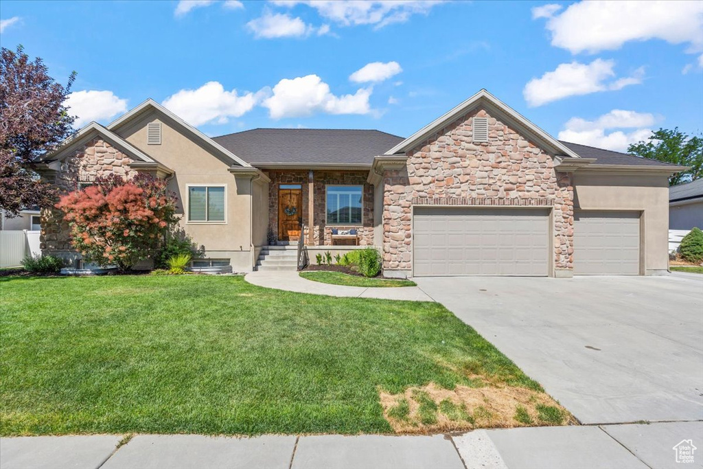 View of front of house featuring a front yard, a garage, stucco siding, driveway, and stone siding