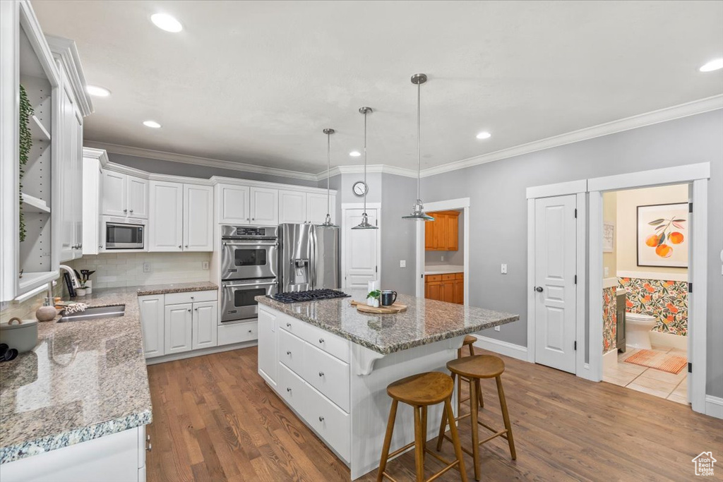 Kitchen with stainless steel appliances, a center island, dark wood finished floors, white cabinets, and ornamental molding
