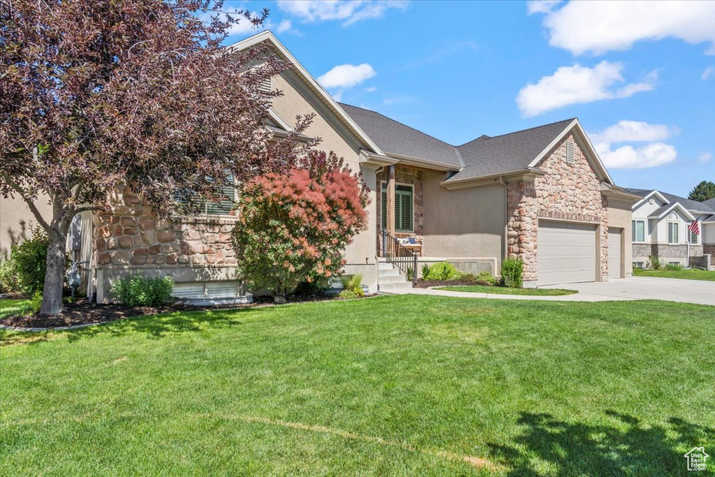 View of front of home with stone siding, driveway, a front yard, and stucco siding