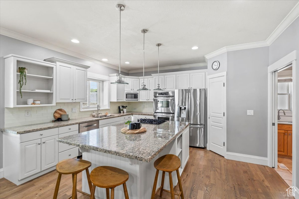 Kitchen with appliances with stainless steel finishes, white cabinets, a kitchen breakfast bar, a center island, and crown molding