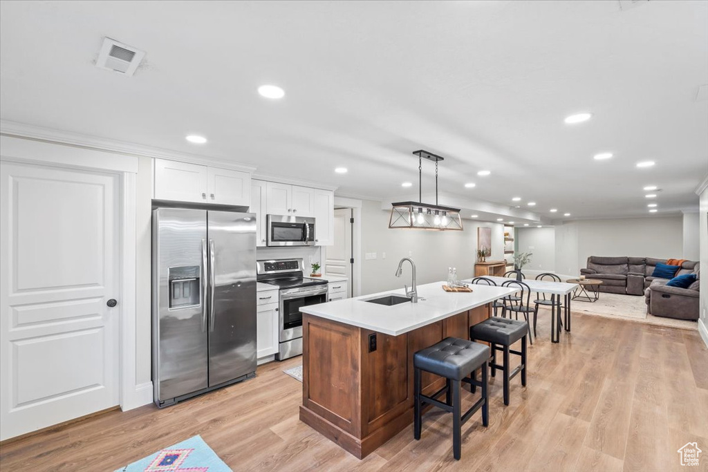 Kitchen featuring stainless steel appliances, a breakfast bar area, white cabinetry, a center island with sink, and recessed lighting