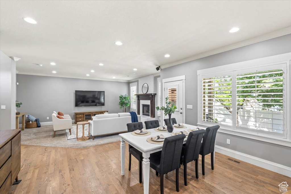 Dining area with recessed lighting, ornamental molding, plenty of natural light, light wood-type flooring, and a large fireplace