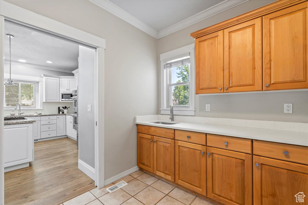 Kitchen featuring appliances with stainless steel finishes, crown molding, light countertops, brown cabinetry, and recessed lighting