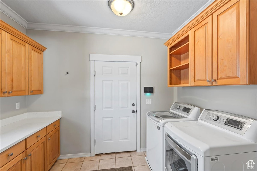 Laundry room featuring washer and dryer, cabinet space, ornamental molding, and light tile patterned floors