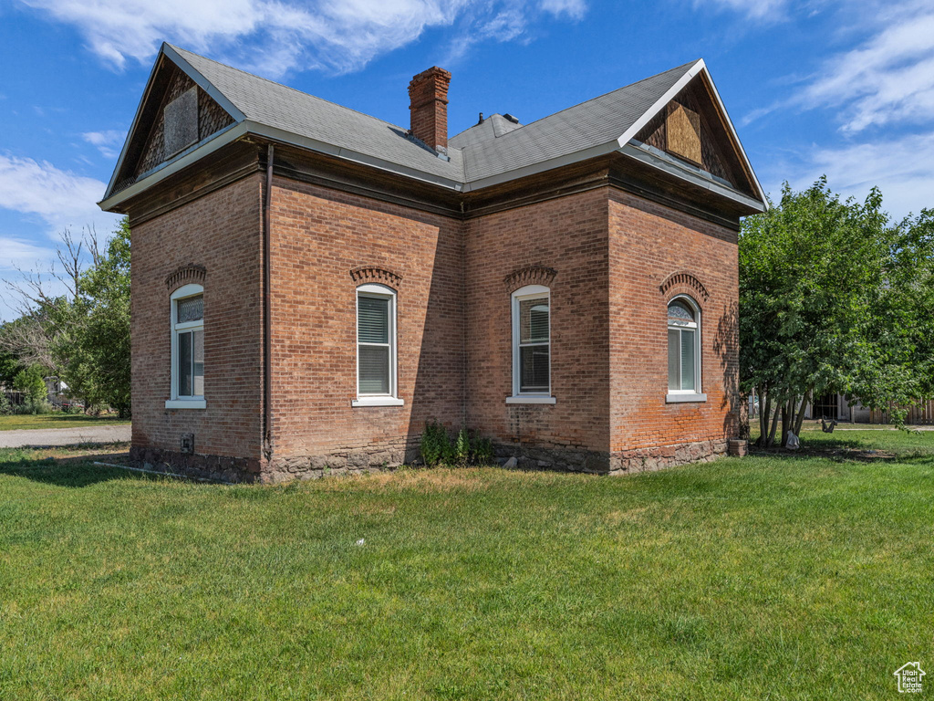 View of side of property featuring brick siding, a chimney, and a lawn