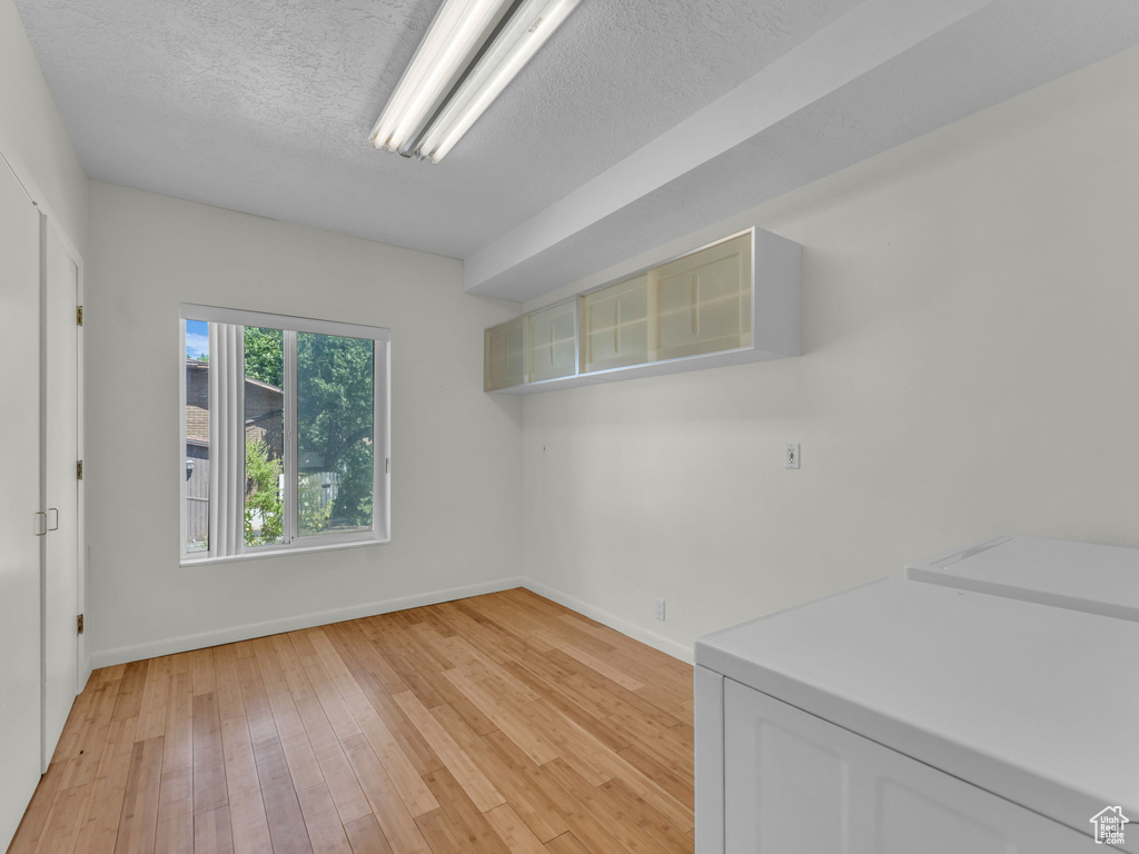 Empty room with washer / clothes dryer, light wood-style flooring, and a textured ceiling