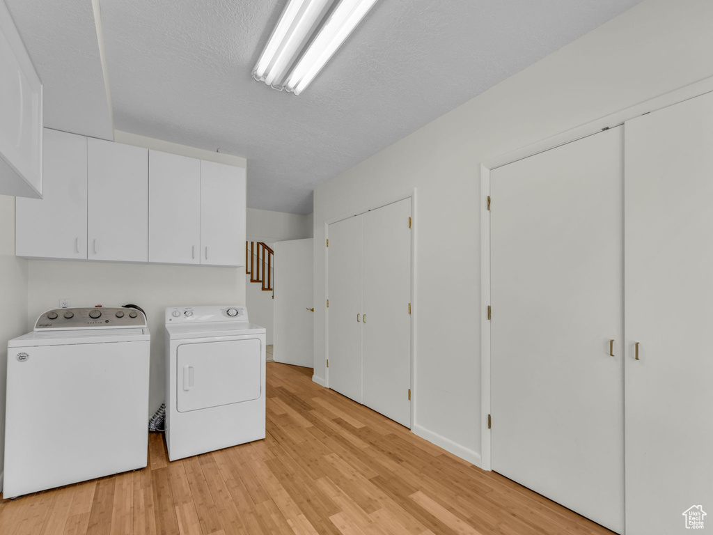 Laundry area with independent washer and dryer, cabinet space, and light wood finished floors