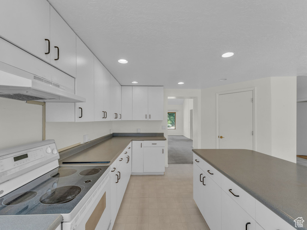 Kitchen featuring white electric range oven, range hood, dark countertops, recessed lighting, and white cabinetry