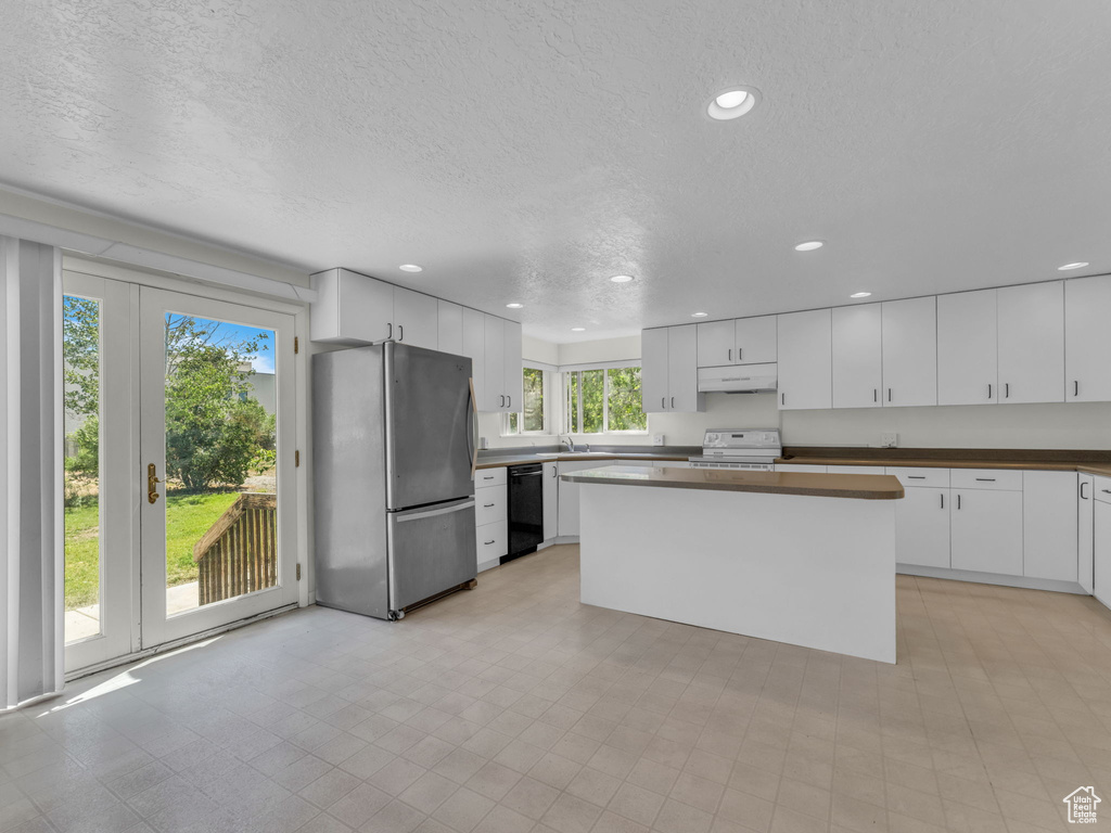 Kitchen with freestanding refrigerator, range, under cabinet range hood, recessed lighting, and a textured ceiling