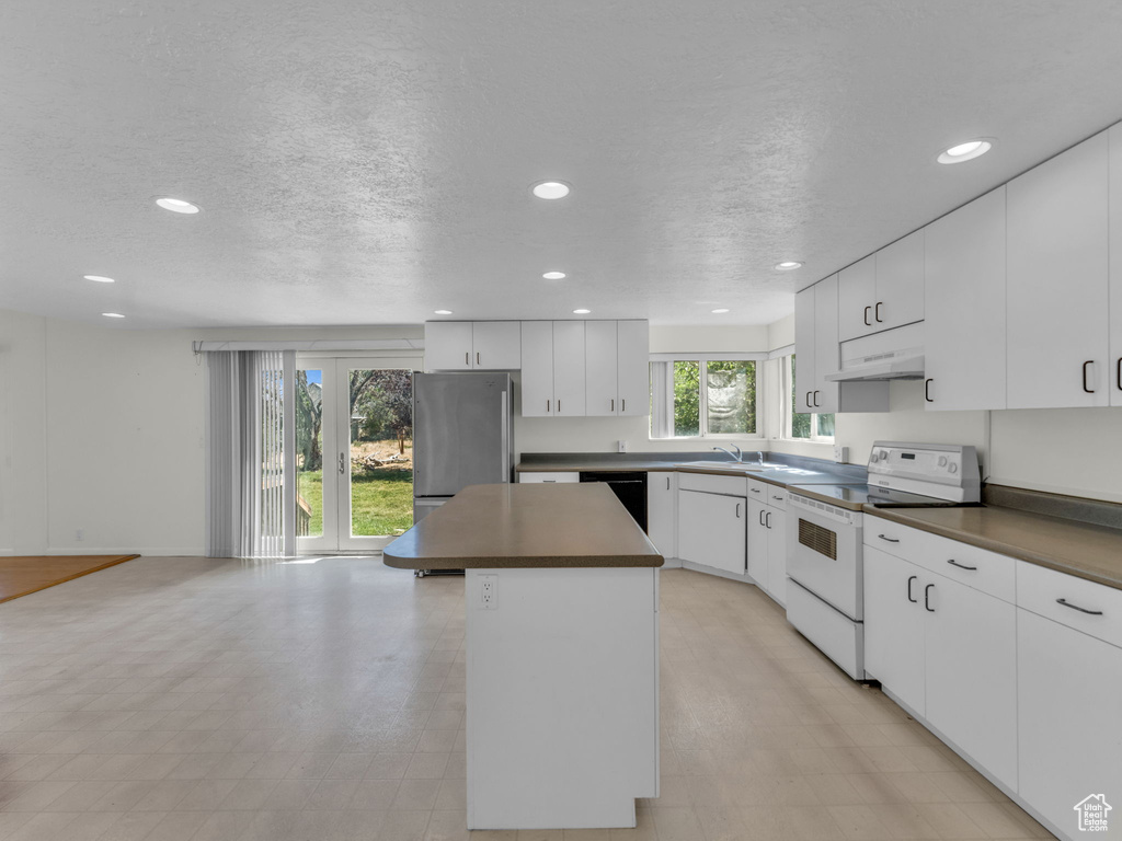 Kitchen with electric stove, freestanding refrigerator, recessed lighting, a center island, and under cabinet range hood