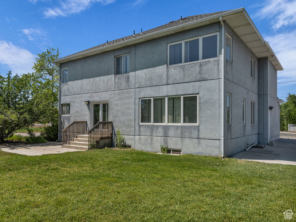 Rear view of house featuring stucco siding, a lawn, and a patio