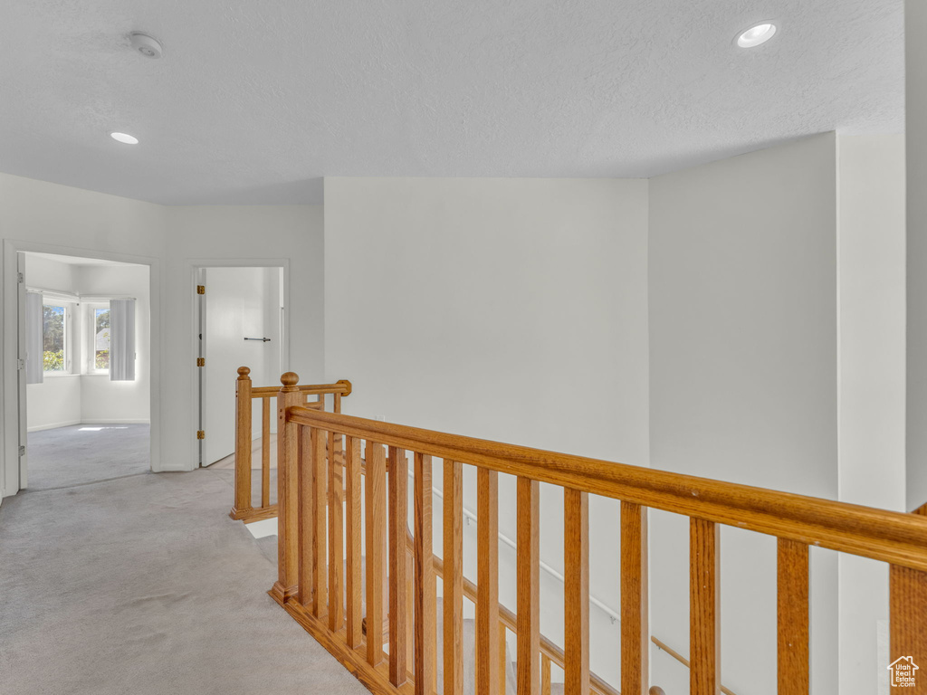 Corridor featuring an upstairs landing, recessed lighting, light carpet, and a textured ceiling