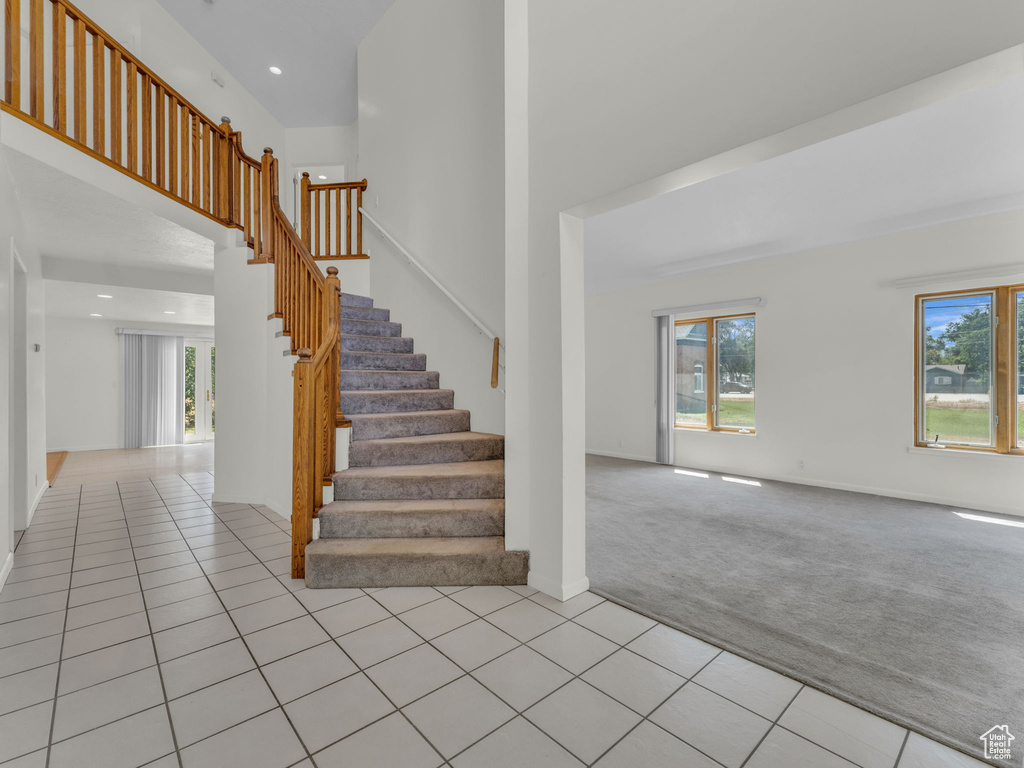 Stairway with healthy amount of natural light, a towering ceiling, carpet, tile patterned flooring, and recessed lighting