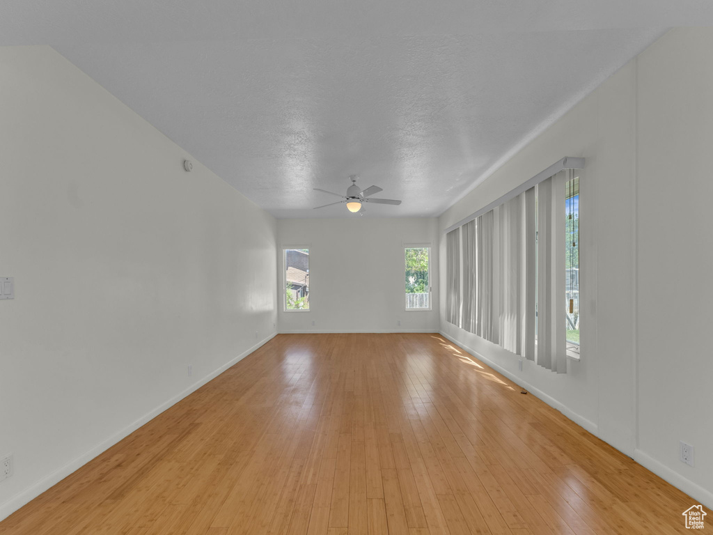 Unfurnished room with a ceiling fan, light wood-style floors, and a textured ceiling