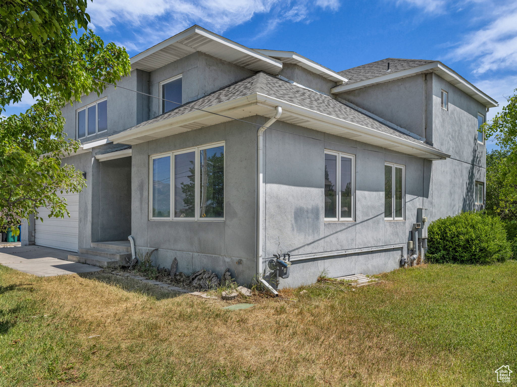 View of side of home featuring a shingled roof, a yard, and stucco siding