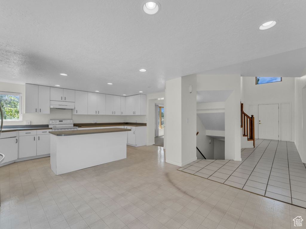 Kitchen with under cabinet range hood, white range with electric cooktop, dark countertops, white cabinetry, and a center island