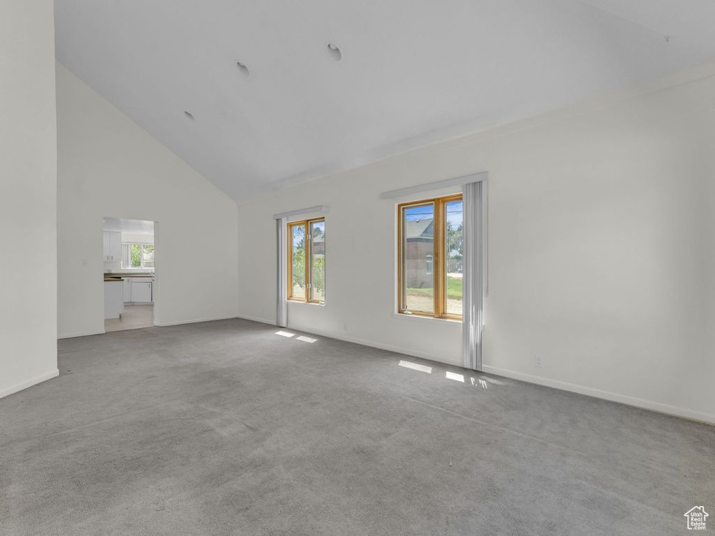 Unfurnished living room with high vaulted ceiling, light colored carpet, and plenty of natural light