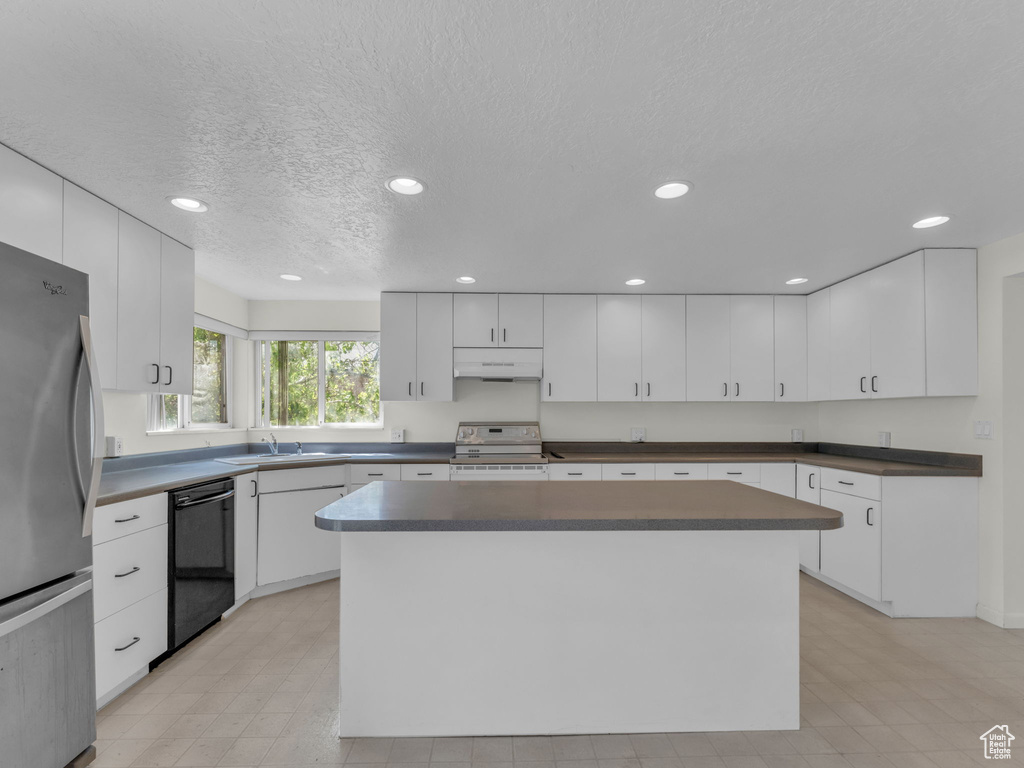 Kitchen featuring freestanding refrigerator, electric range oven, dishwasher, dark countertops, and a textured ceiling