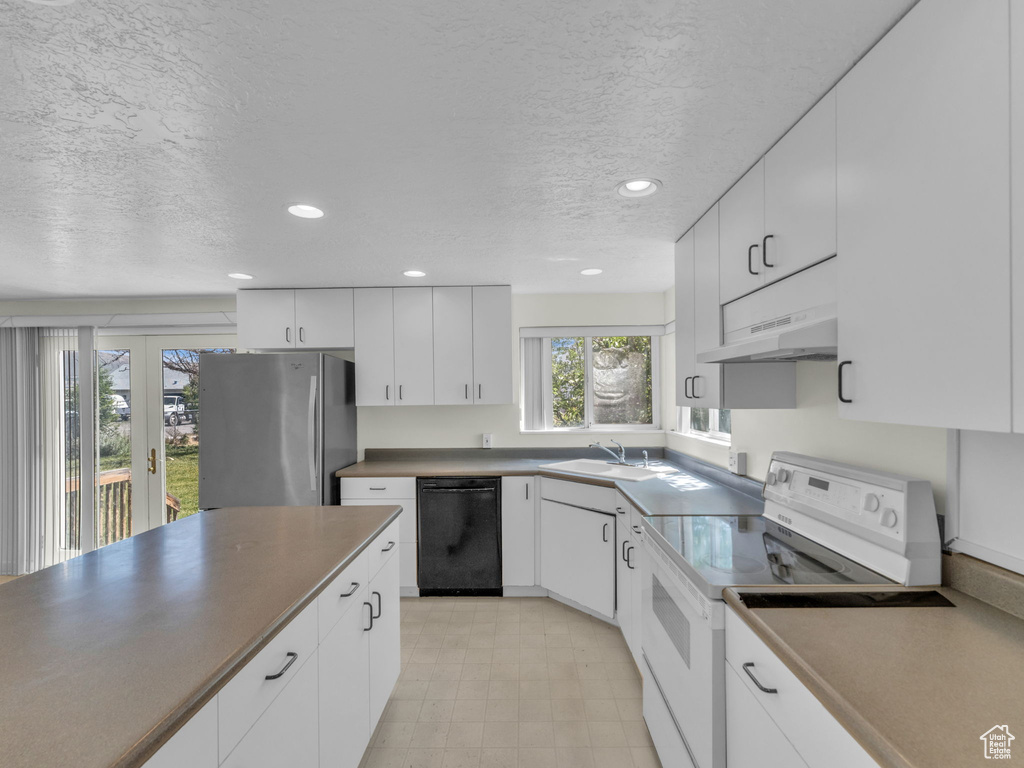 Kitchen with black dishwasher, white electric stove, freestanding refrigerator, under cabinet range hood, and a textured ceiling