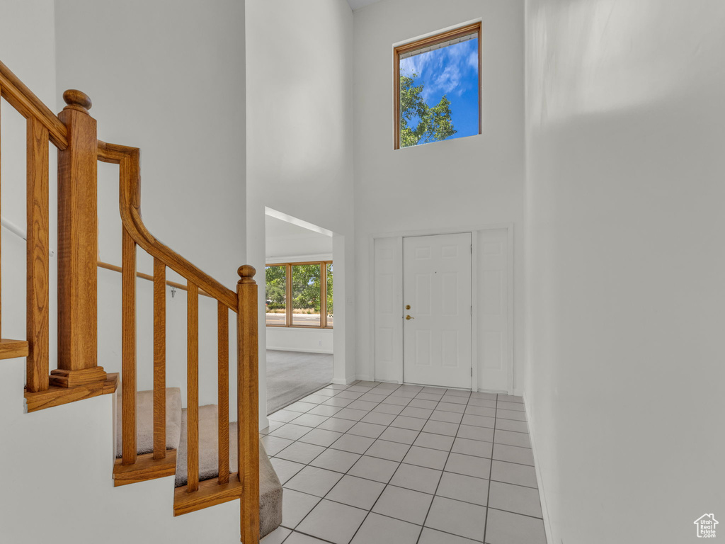 Foyer entrance with stairs, light tile patterned floors, and a high ceiling
