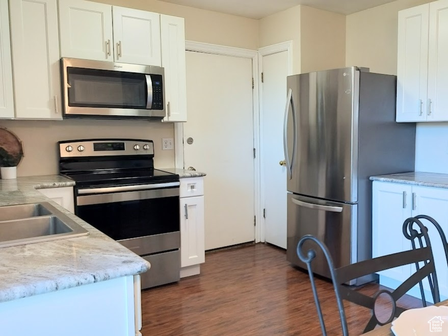Kitchen featuring stainless steel appliances, white cabinetry, dark wood-type flooring, and light stone countertops