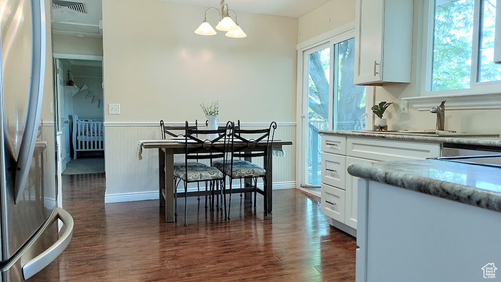 Dining room featuring dark wood-type flooring, a wainscoted wall, a chandelier, and plenty of natural light