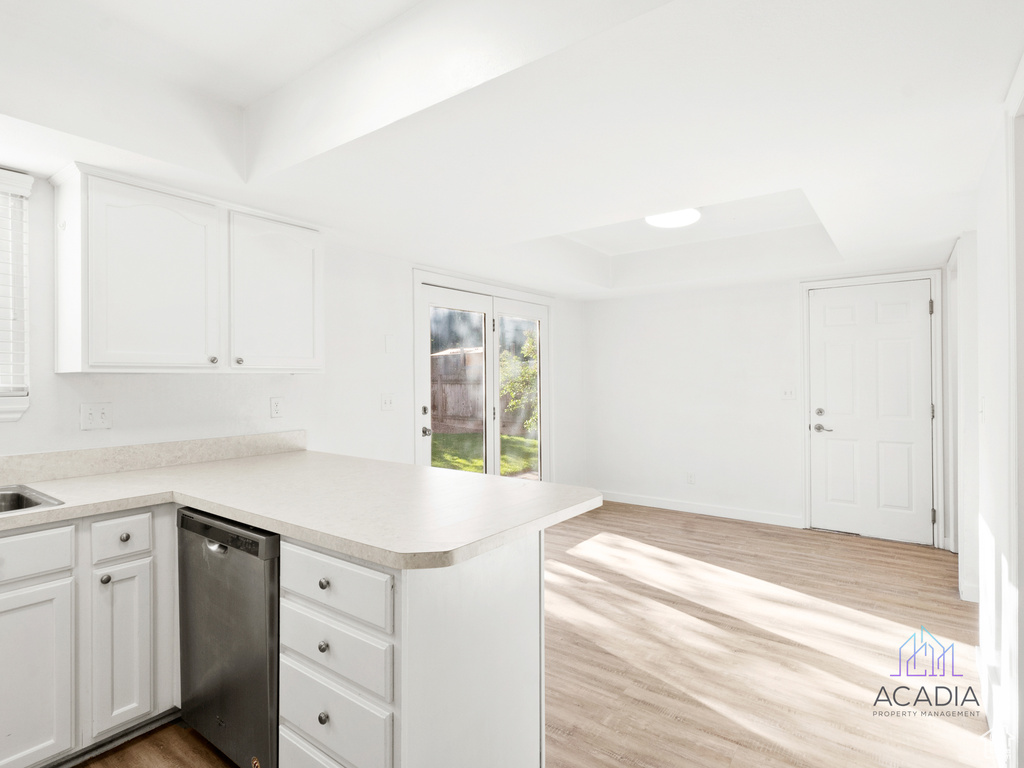 Kitchen featuring stainless steel dishwasher, a raised ceiling, a peninsula, and light wood-style floors