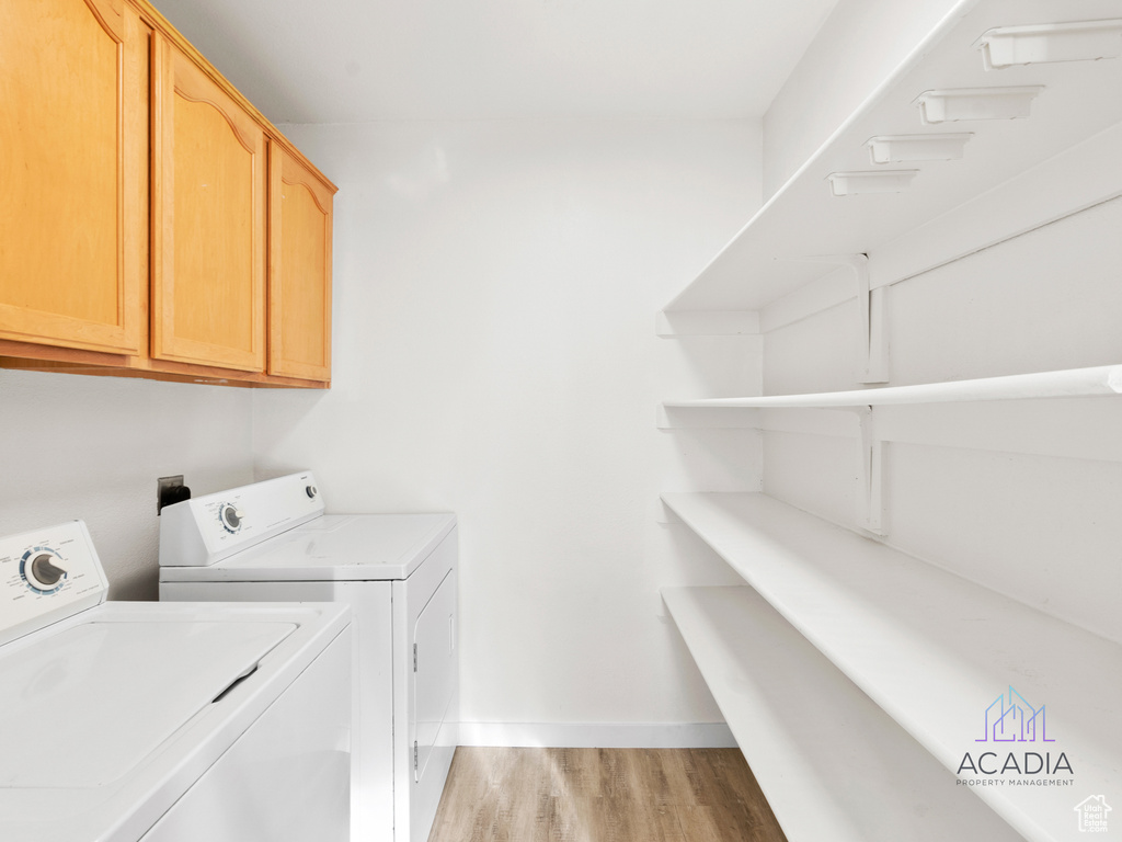 Washroom with cabinet space, washer and dryer, and light wood-type flooring