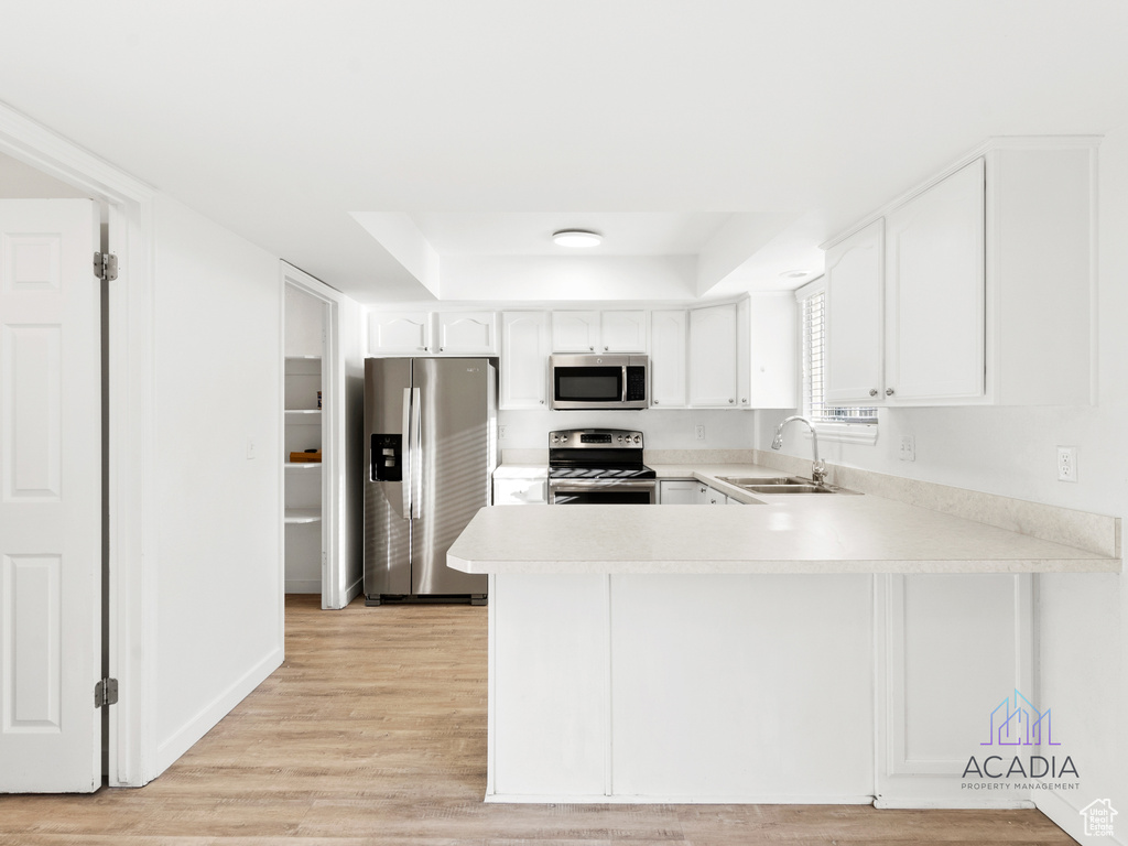Kitchen featuring stainless steel appliances, a tray ceiling, light countertops, a peninsula, and white cabinets