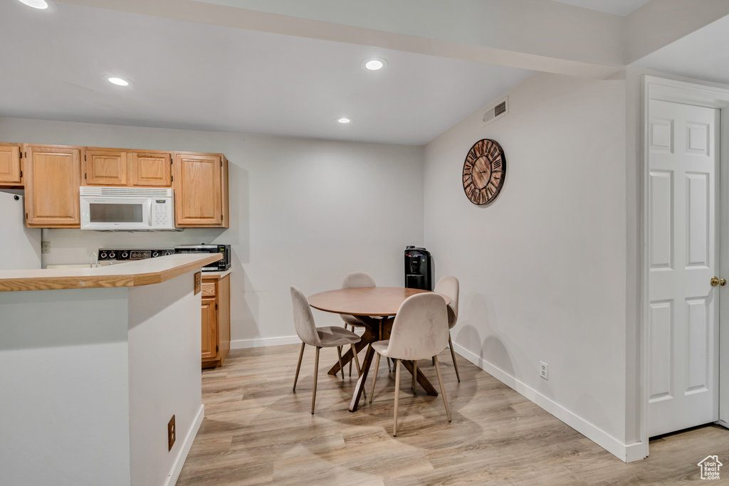 Kitchen with white microwave, refrigerator, recessed lighting, light wood-type flooring, and light brown cabinets