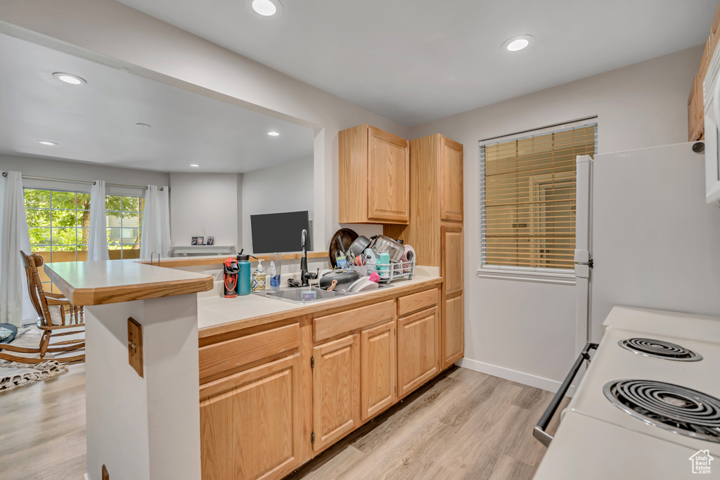 Kitchen with light brown cabinetry, a peninsula, light wood-style flooring, white appliances, and recessed lighting