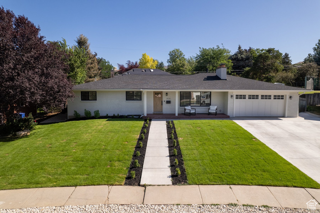 Single story home featuring a front yard, concrete driveway, a garage, a chimney, and brick siding