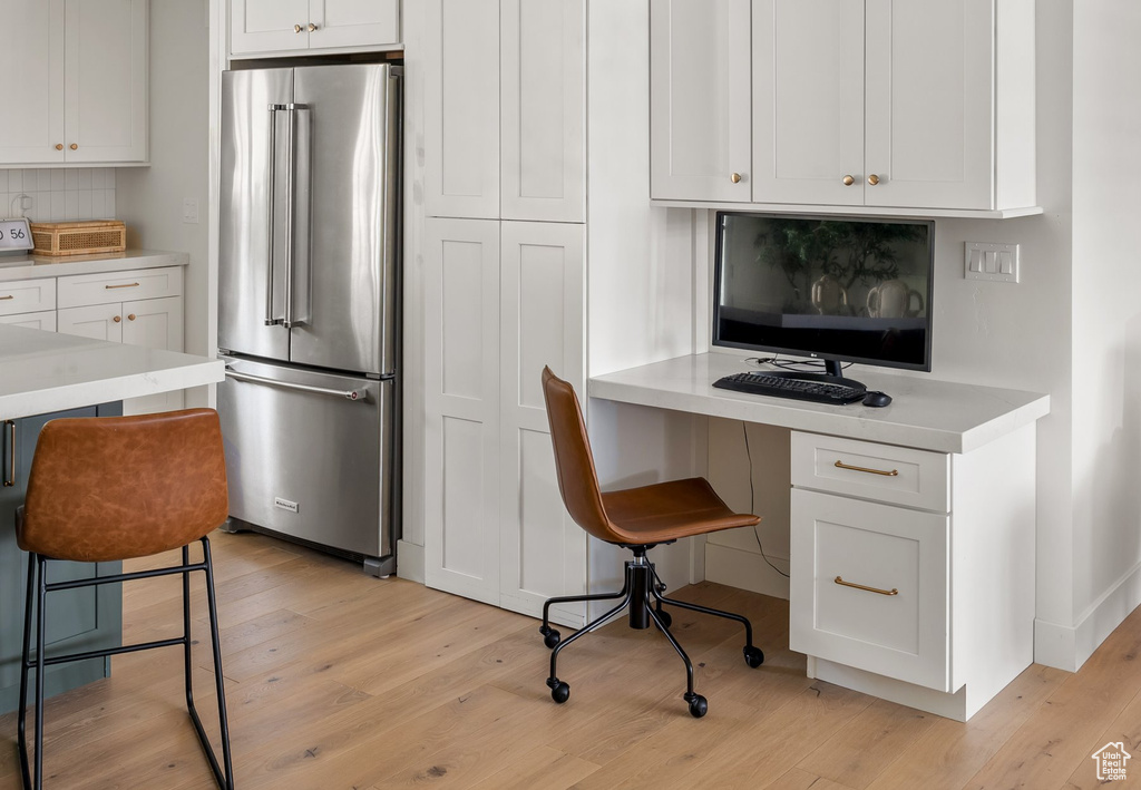 Kitchen featuring high end refrigerator, a kitchen bar, light countertops, light wood finished floors, and built in desk