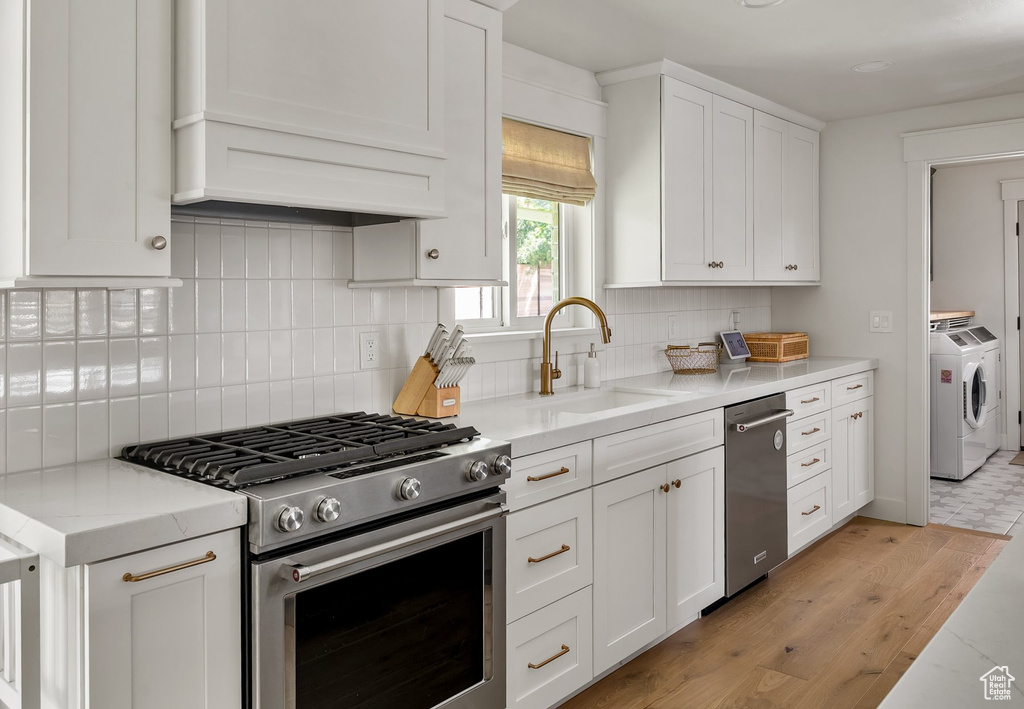 Kitchen featuring appliances with stainless steel finishes, white cabinets, separate washer and dryer, decorative backsplash, and light wood-type flooring