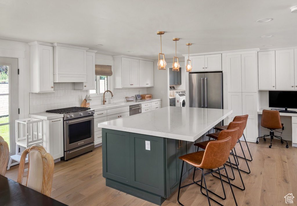 Kitchen with high end appliances, independent washer and dryer, white cabinetry, a center island, and backsplash