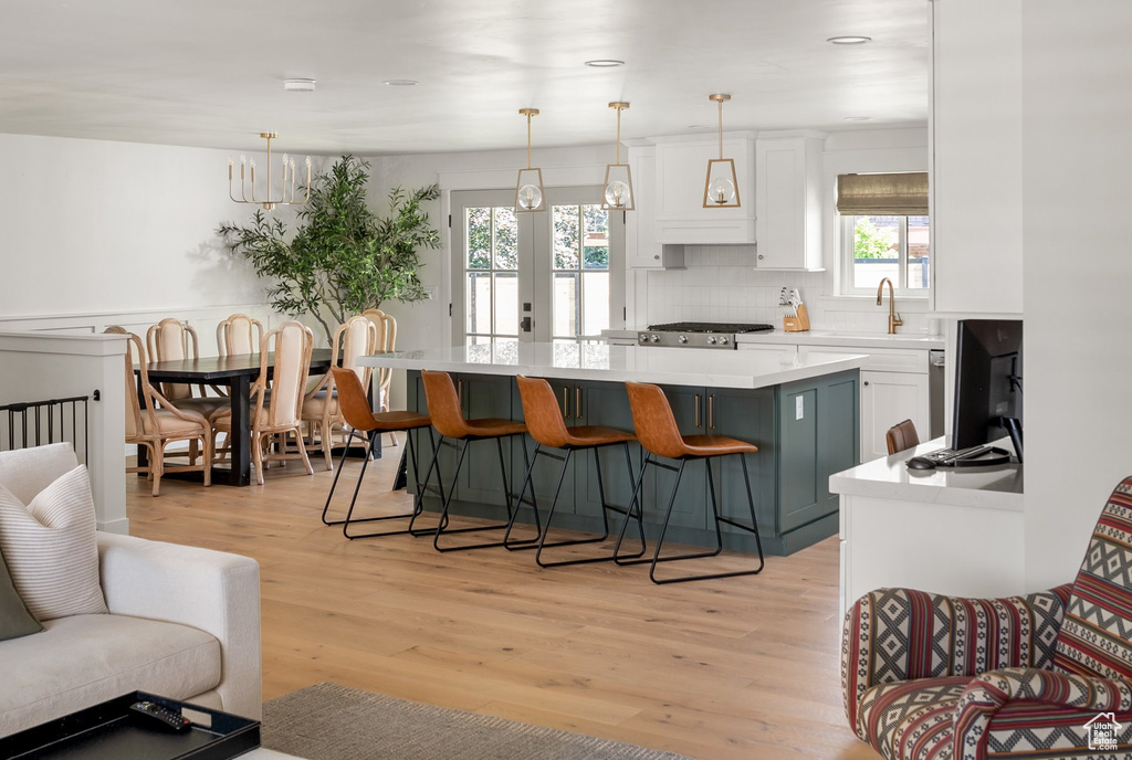 Kitchen with light countertops, a kitchen island, white cabinets, light wood-style flooring, and decorative backsplash