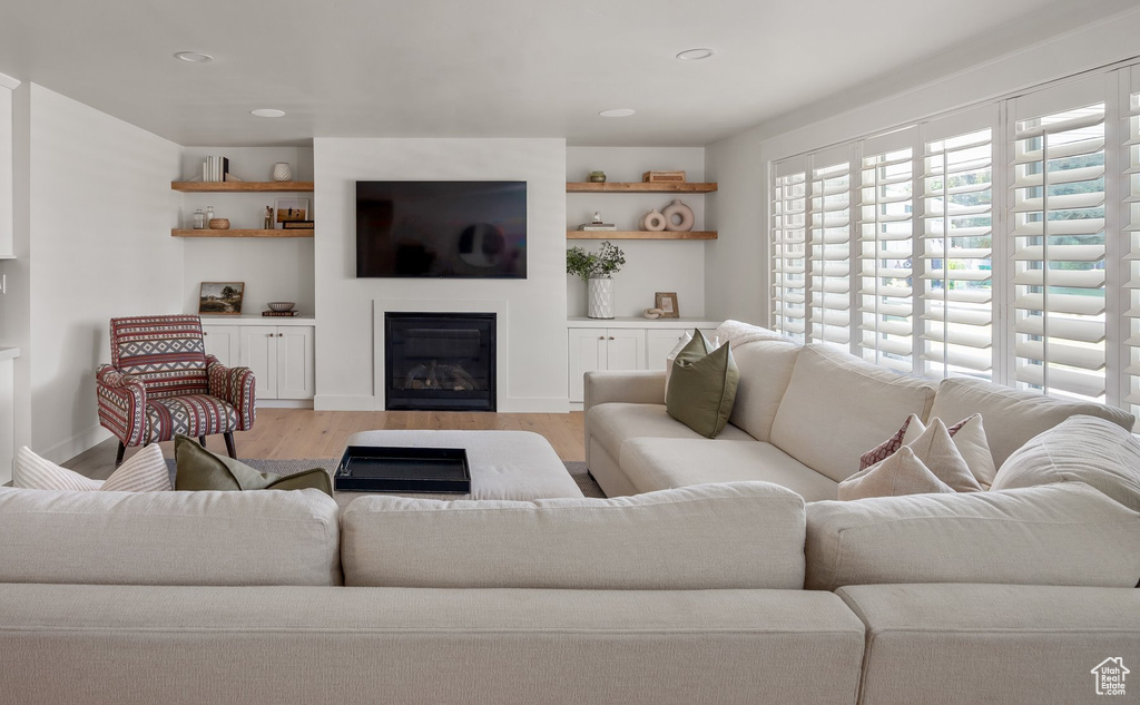 Living room featuring light wood-type flooring, a glass covered fireplace, and recessed lighting