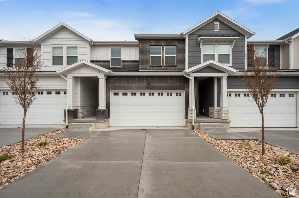 View of front of house with board and batten siding, a garage, concrete driveway, and brick siding