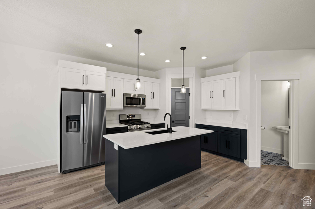 Kitchen featuring stainless steel appliances, light wood-style flooring, white cabinets, a center island with sink, and recessed lighting