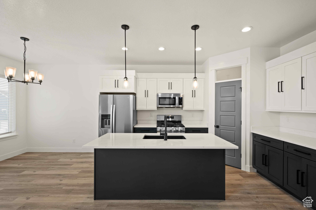 Kitchen with appliances with stainless steel finishes, a chandelier, white cabinets, light countertops, and light wood finished floors