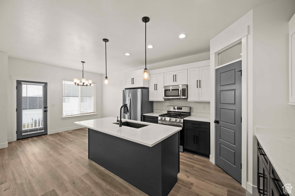 Kitchen featuring appliances with stainless steel finishes, a chandelier, light wood-style floors, a kitchen island with sink, and white cabinets