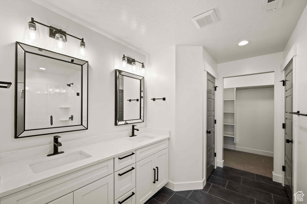 Bathroom featuring double vanity, a shower stall, a spacious closet, a textured ceiling, and recessed lighting