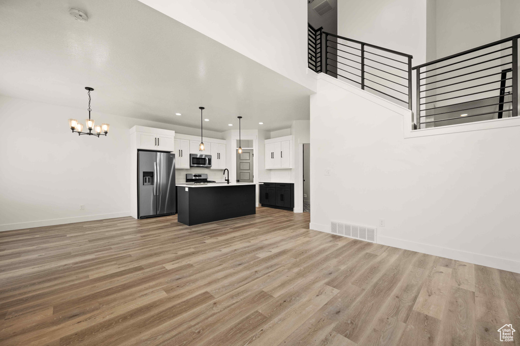 Kitchen featuring appliances with stainless steel finishes, a chandelier, open floor plan, white cabinetry, and light wood-type flooring
