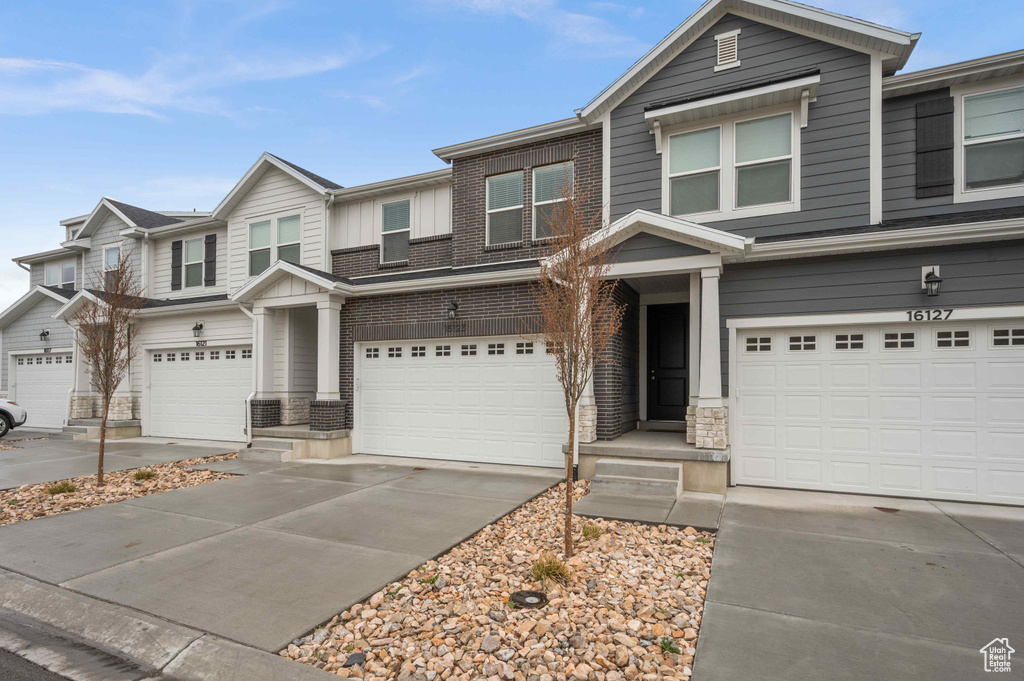 View of front of property featuring board and batten siding, stone siding, an attached garage, and driveway