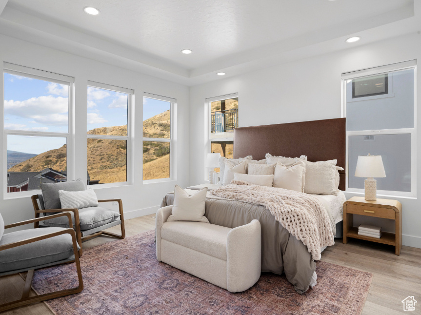 Bedroom with light wood finished floors, recessed lighting, a mountain view, and a raised ceiling