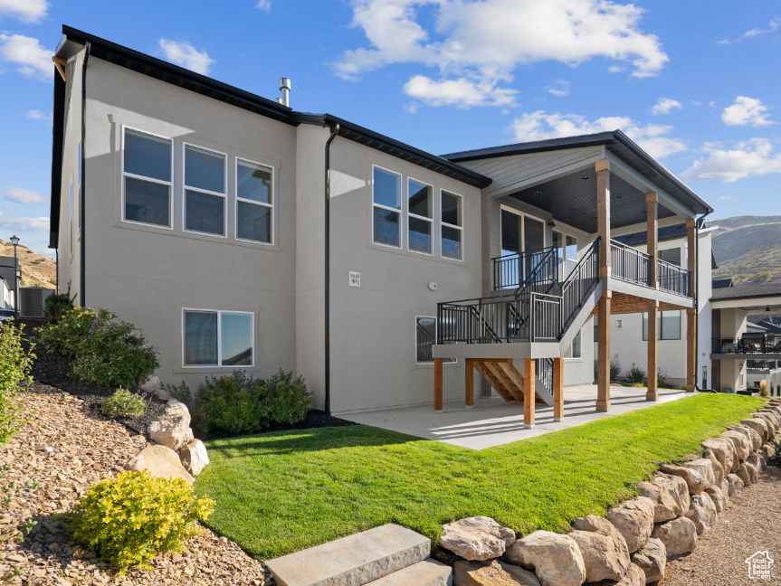 Back of property featuring stucco siding, a patio area, stairs, and a yard