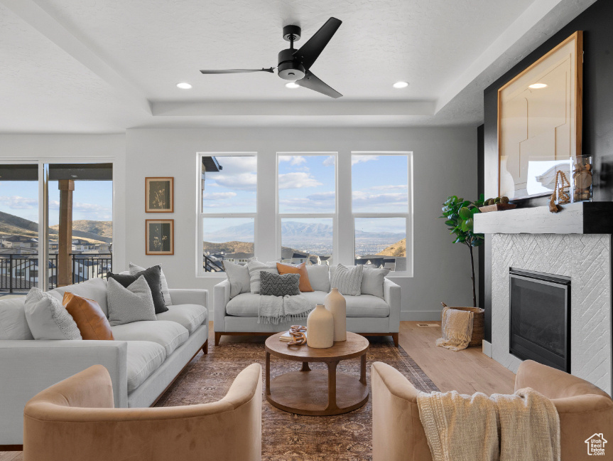 Living room featuring a raised ceiling, wood finished floors, a ceiling fan, a tiled fireplace, and recessed lighting