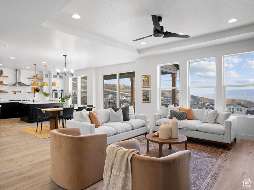 Living area featuring a raised ceiling, a chandelier, light wood-type flooring, a ceiling fan, and recessed lighting