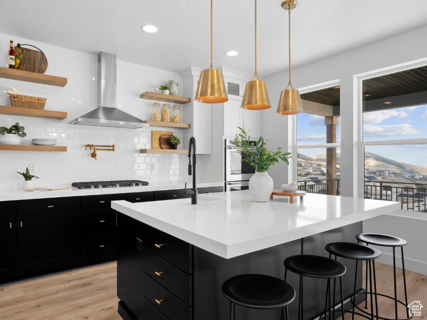 Kitchen featuring wall chimney range hood, dark cabinetry, open shelves, gas cooktop, and recessed lighting
